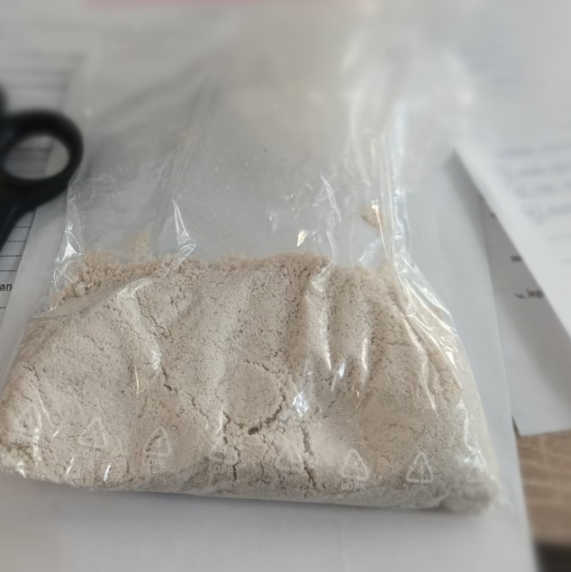 Zamknięta torebka plastikowa z szarym proszkiem leży na biurku obok nożyczek i dokumentów.