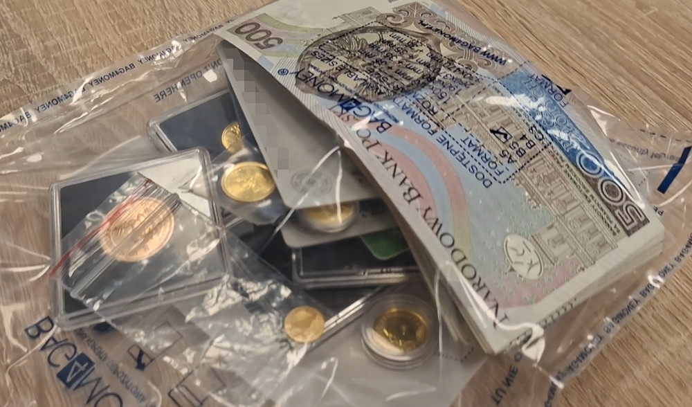 Zestaw monet w kapslach oraz banknot 500 zł w przezroczystej torebce na tle drewnianego blatu.