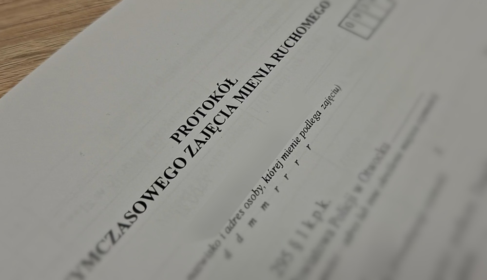 Dokument z nagłówkiem „PROTOKÓŁ ZAJĘCIA MIENIA RUCHOMEGO” leży na drewnianym stole.