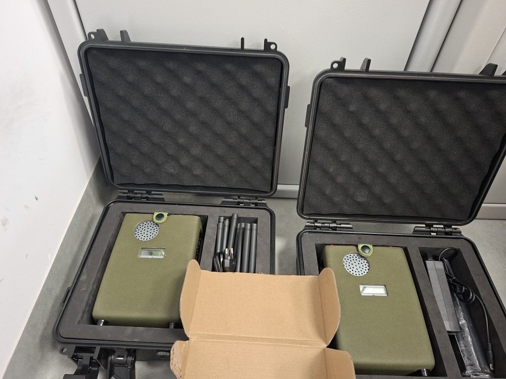 Dwa zamknięte walizki ochronne z elektroniką, w tym zielone urządzenia i akcesoria, leżą na szarej powierzchni.