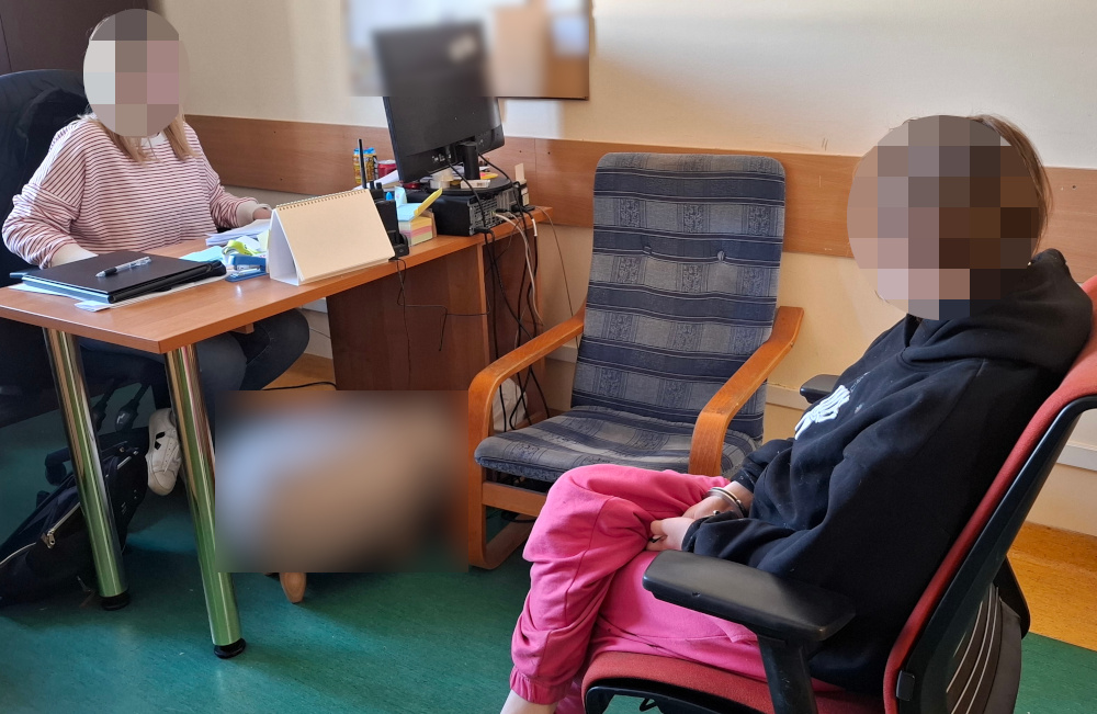 Kobieta w bluzie siedzi na krześle w biurze, a druga osoba w koszulce rozmawia z nią przy biurku.