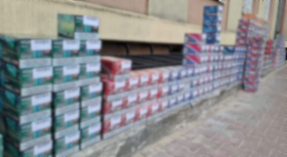 Stosy kartonów z różnymi produktami ustawione wzdłuż ściany budynku na chodniku.