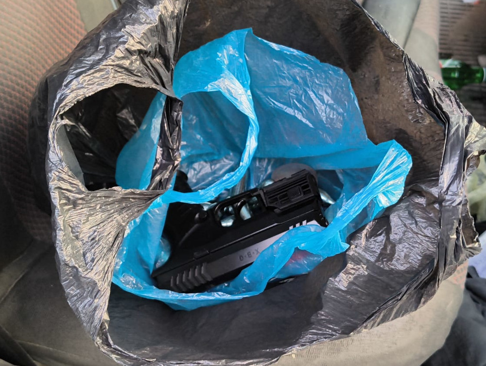 Czarna torba z niebieską folią, w której widoczny jest pistolet i kilka metalowych przedmiotów.