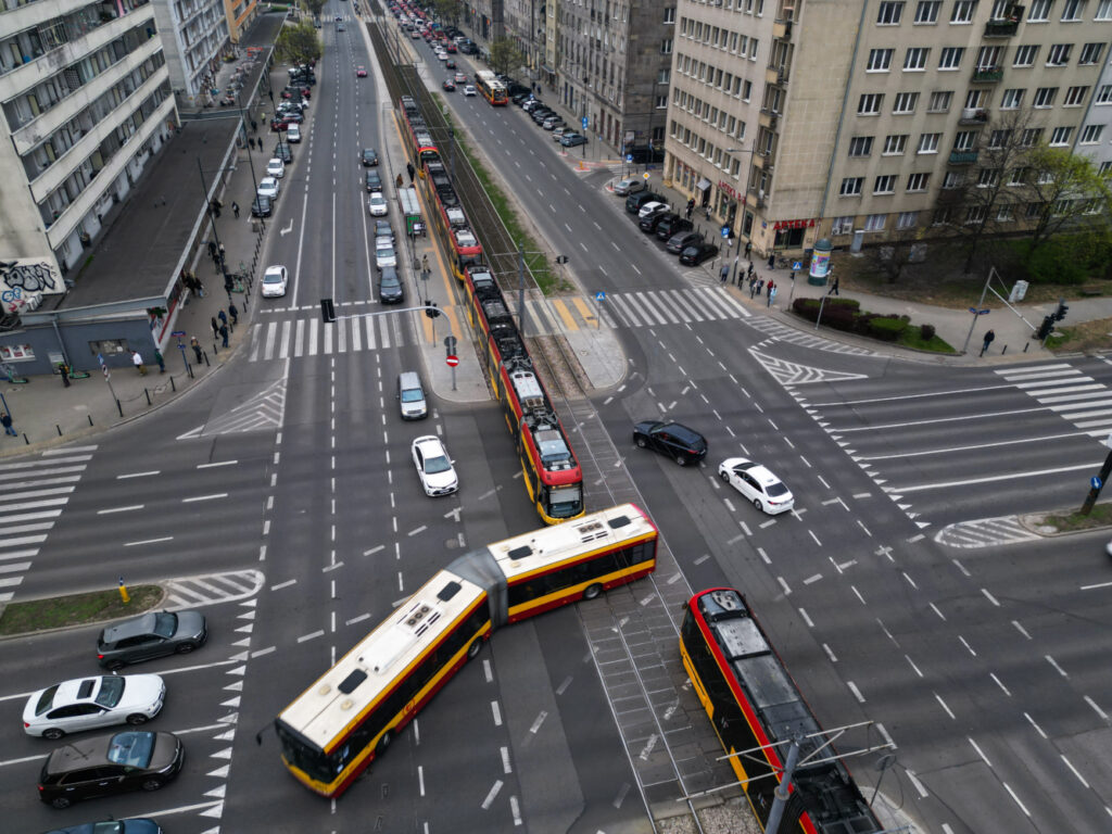 Tramwaj skręcający na skrzyżowaniu z ruchem samochodowym w miejskim otoczeniu.