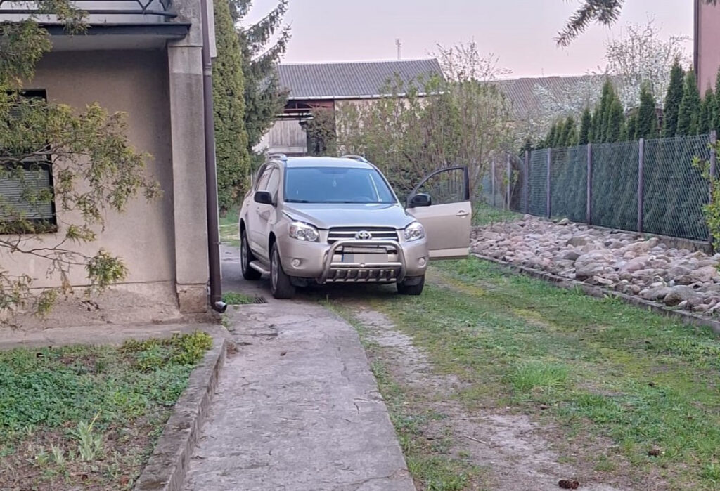 Srebrny SUV zaparkowany na wąskiej drodze przed budynkiem mieszkalnym, z otwartymi drzwiami od strony pasażera.