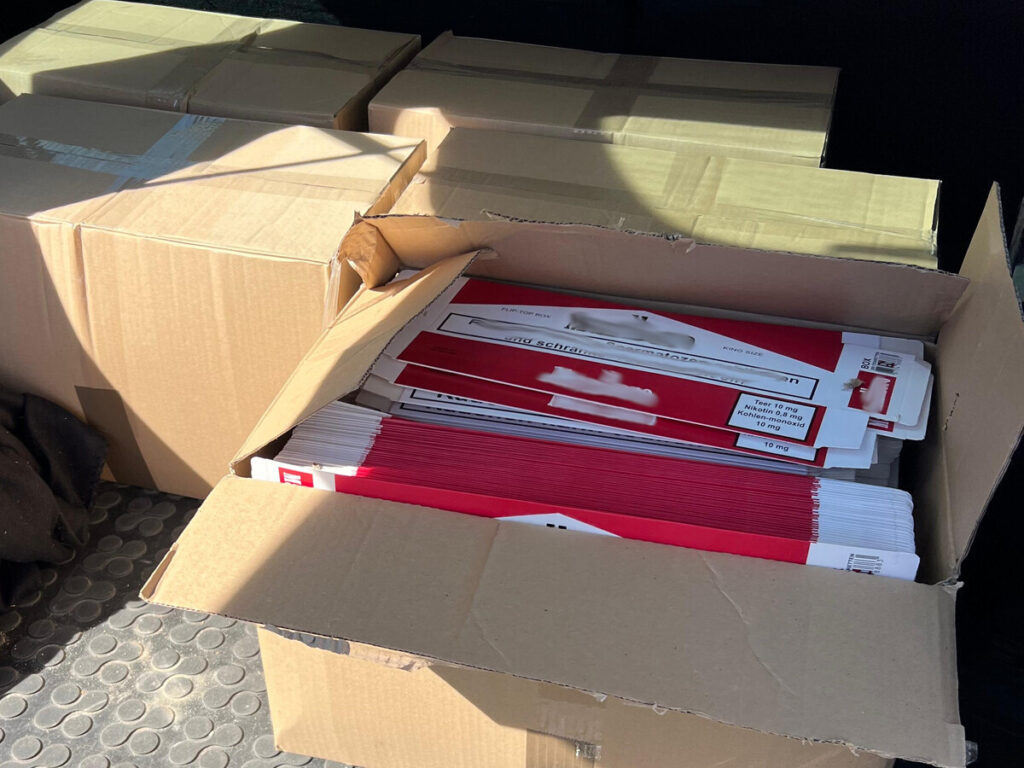 Otwarte kartony w bagażniku, wypełnione kolorowymi opakowaniami z etykietami medycznymi.