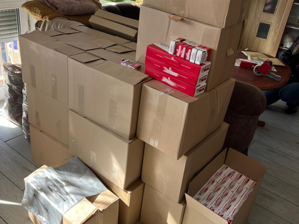 Stosy kartonowych pudełek oraz opakowań w kolorze czerwonym na podłodze w jasnym pomieszczeniu.