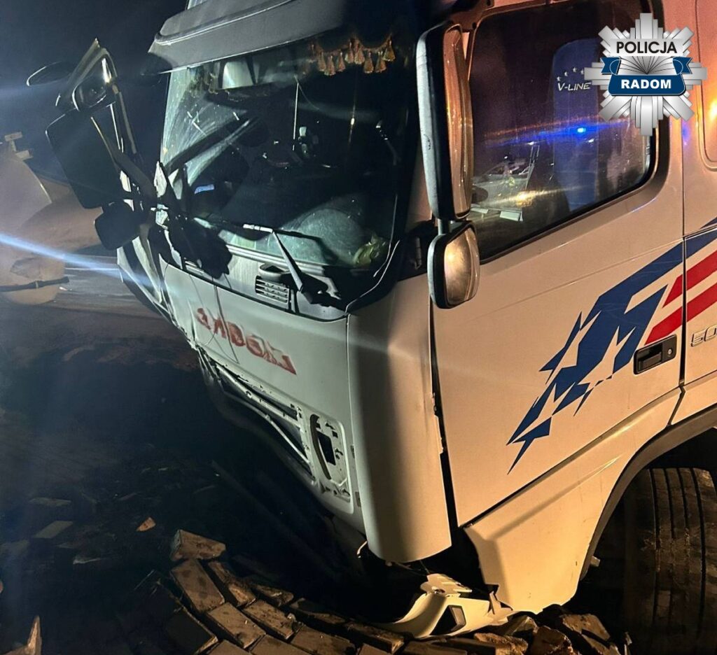 Zniszczony ciężarówka z wgniecioną kabiną leży na boku na drodze, otoczona przez światła policyjne.