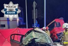 Zniszczony samochód osobowy po wypadku drogowym, otoczony przez strażaków i czerwony namiot.