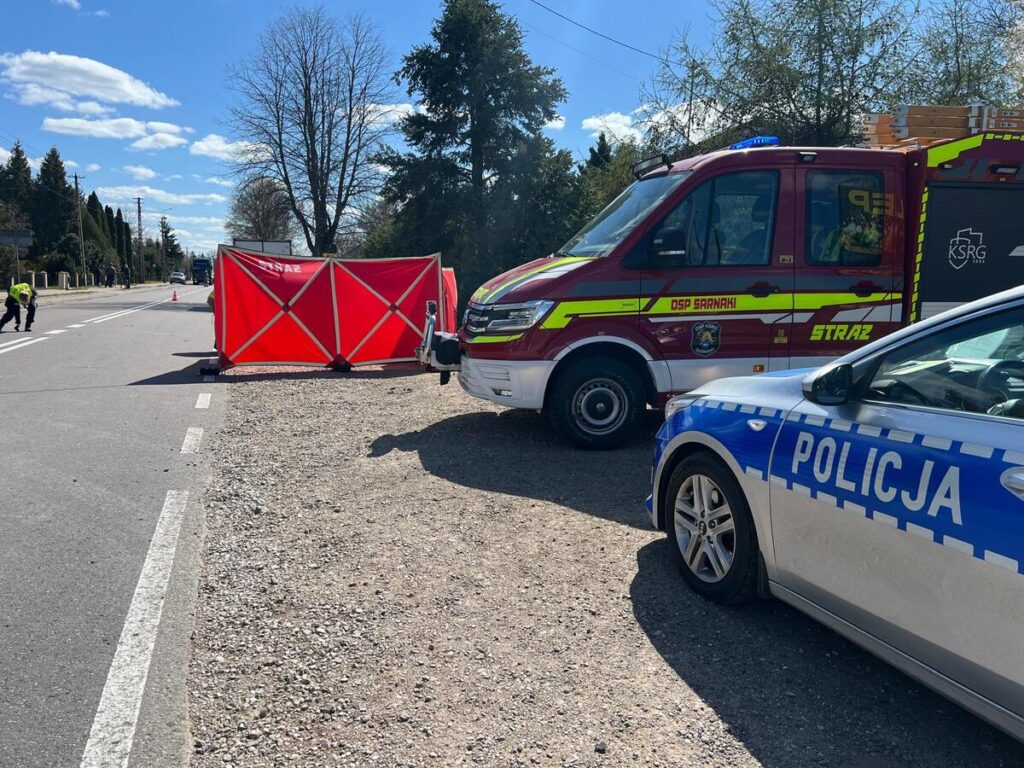 Na drodze ustawiony czerwony namiot, obok stoją radiowóz policji i wóz strażacki. Funkcjonariusze prowadzą działania.