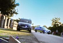 Uszkodzony skuter elektryczny leży na poboczu drogi, obok przejeżdżających radiowozów policyjnych.