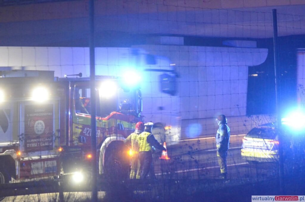 Pojazdy służb ratunkowych z włączonymi sygnałami świetlnymi na drodze, podczas interwencji nocnej.