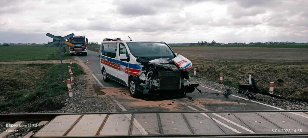 Uszkodzony pojazd ratunkowy stoi na torach kolejowych, obok widać wóz strażacki oraz znaki ostrzegawcze.