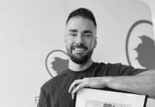 Mężczyzna z brodą uśmiecha się, trzymając w rękach ramkę z certyfikatem w jasnym wnętrzu.