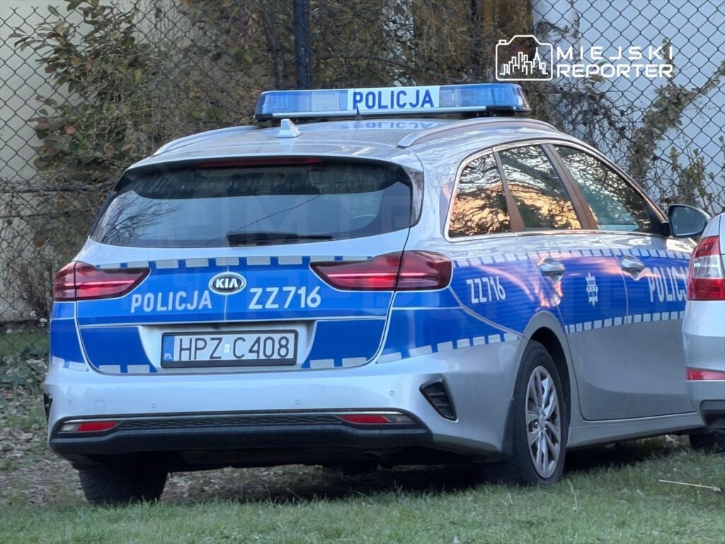 Policyjny samochód marki Kia zaparkowany na trawniku, z widocznym oznaczeniem "POLICJA ZZ716" i numerem rejestracyjnym HPZ C408.