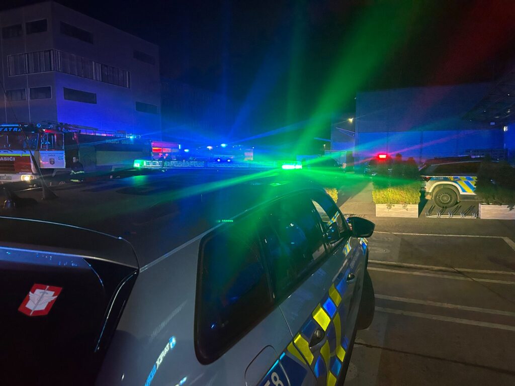 Nocna akcja służb ratunkowych z niebieskimi i zielonymi światłami w pobliżu budynku przemysłowego.