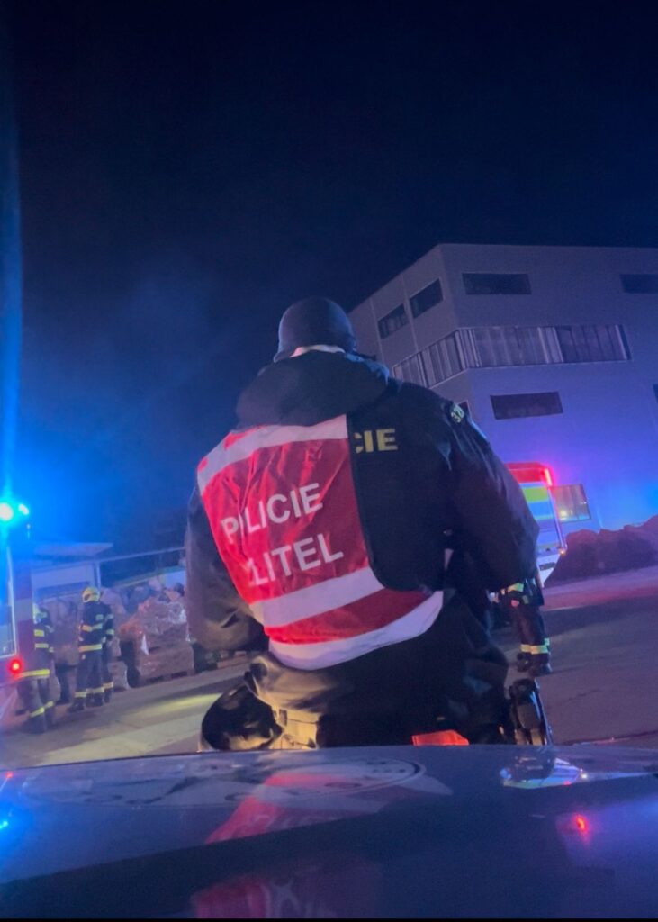 Policjant w kamizelce odblaskowej obserwuje sytuację przy miejscu zdarzenia w nocy, w tle widać radiowóz.