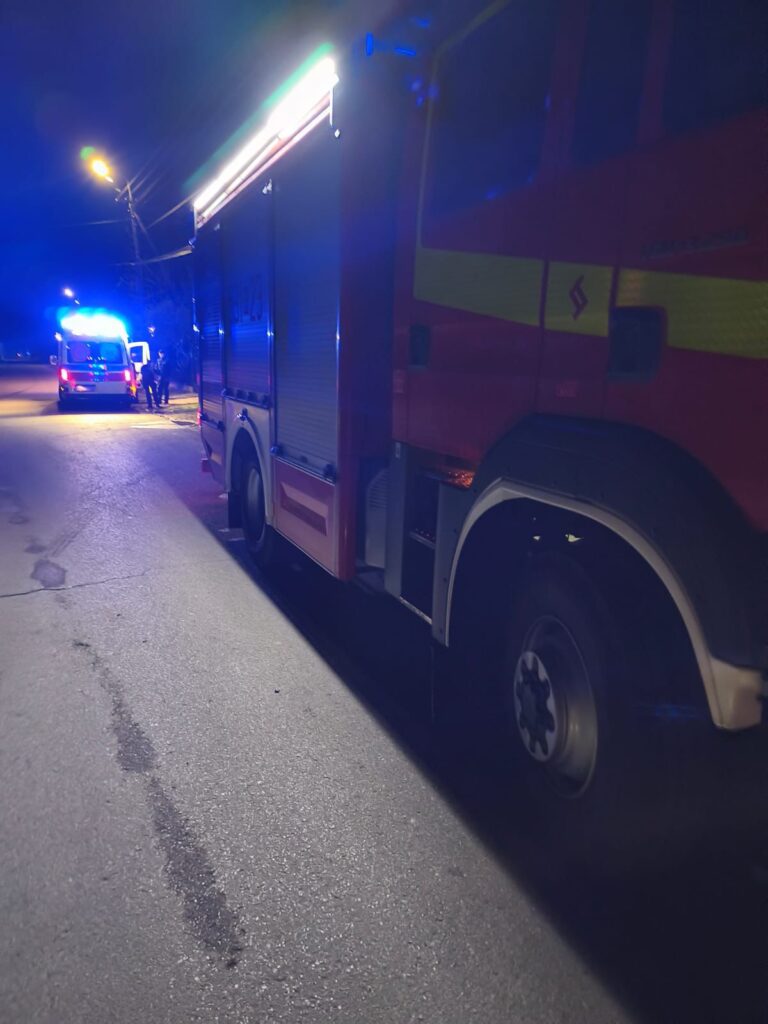 Czerwony wóz strażacki z włączonymi sygnalizatorami świetlnymi stoi na nocnej ulicy, obok drugiego pojazdu ratunkowego.