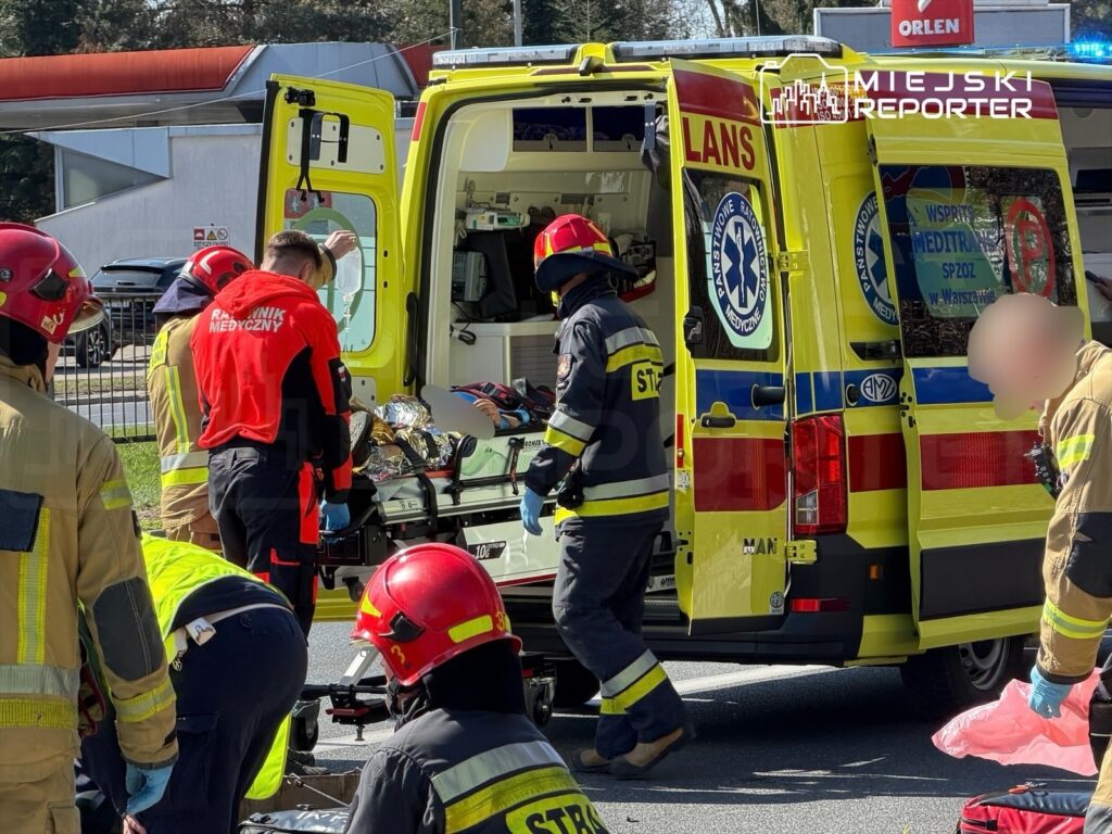 Grupa ratowników medycznych i strażaków przygotowuje nosze w pobliżu karetki pogotowia na ulicy.