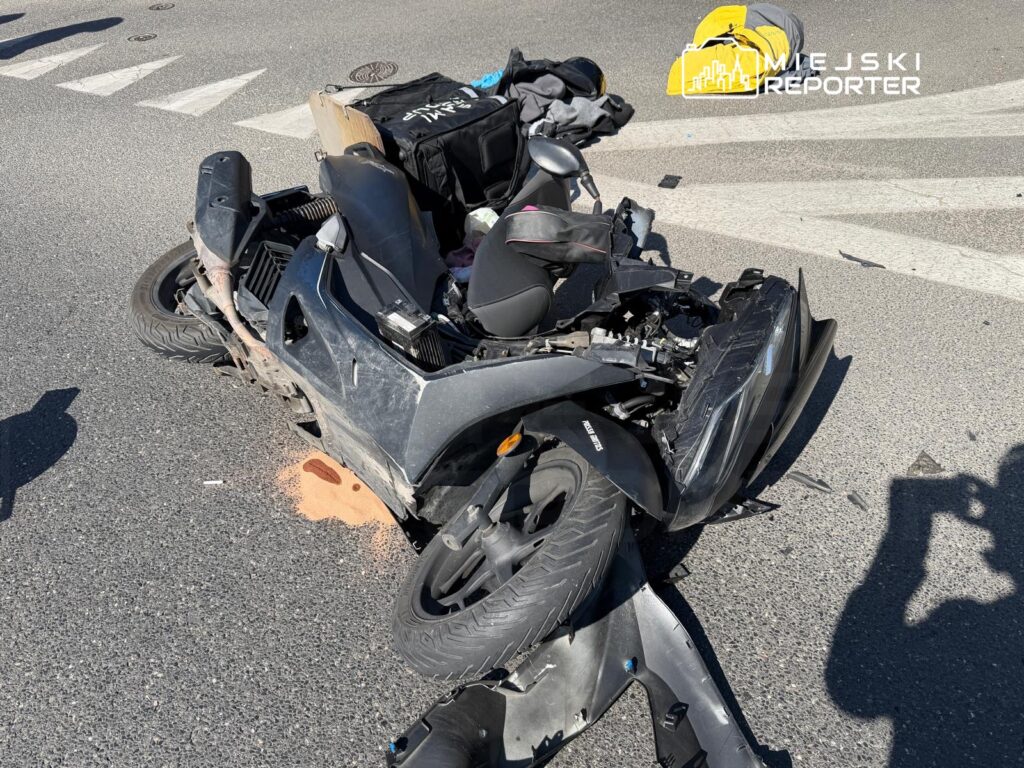 Zniszczony skuter leży na jezdni, obok widać plamę cieczy oraz fragmenty uszkodzonej obudowy.
