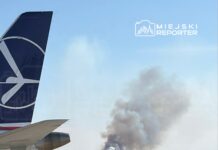 Samolot z logo linii lotniczej na pierwszym planie, w tle widoczny dym unoszący się z pożaru na horyzoncie.