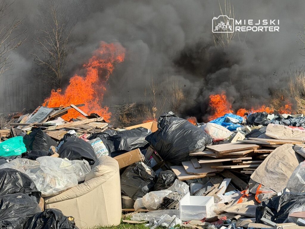 Ognisko pożaru wydobywa się z sterty odpadów, w tle unosi się gęsty, czarny dym.