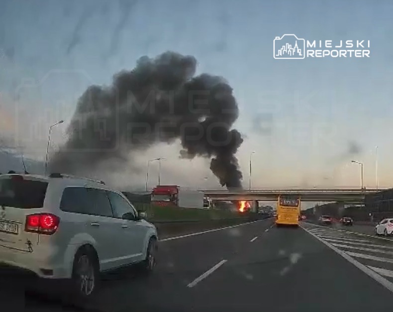 Czarny dym unoszący się z pożaru w pobliżu autostrady, obok ruchliwych pojazdów.