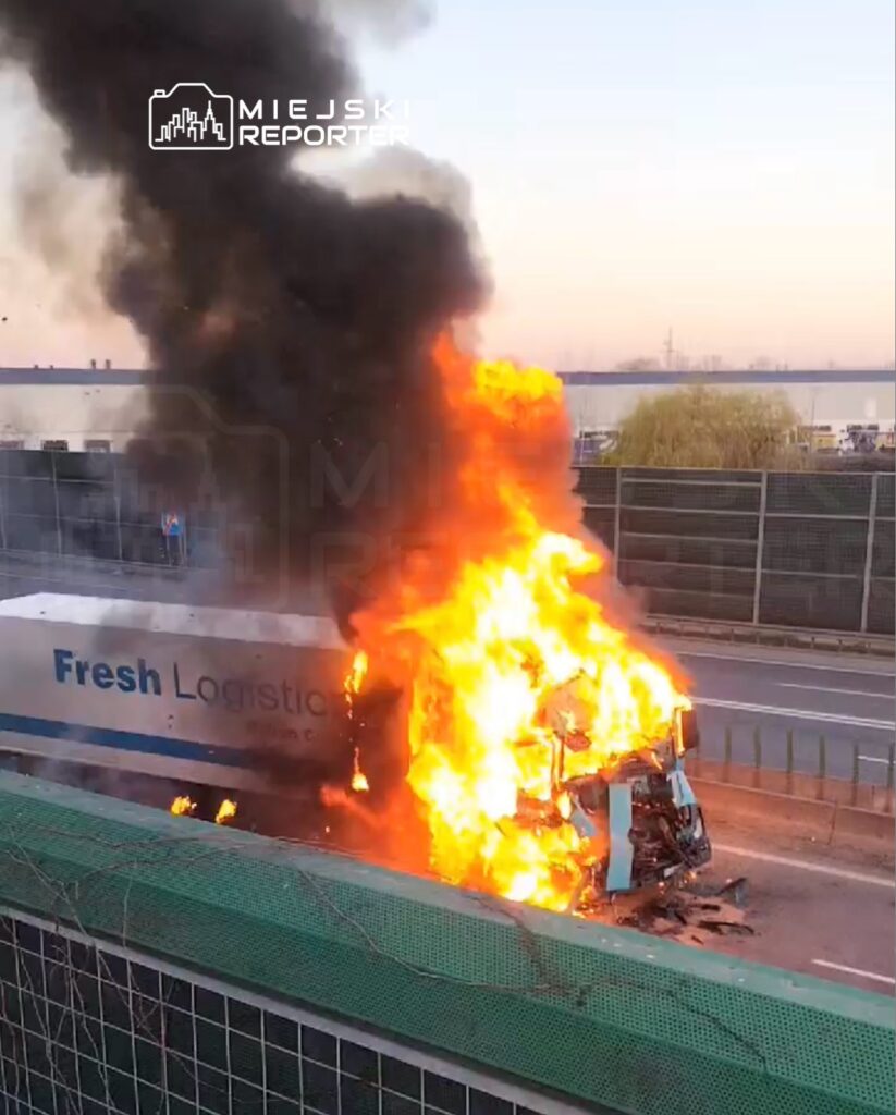 Cysterna z napisem "Fresh Logistics" płonie na drodze, wydobywając czarny dym i płomienie.