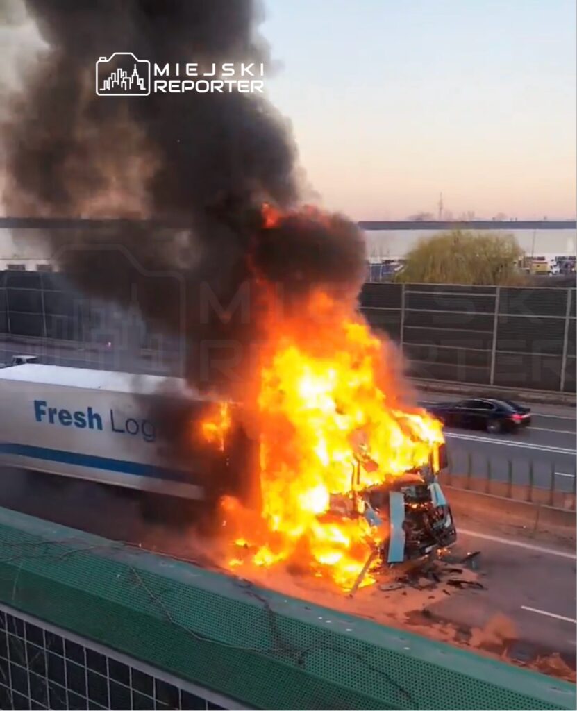 Cysterna transportowa płonąca na autostradzie, otoczona chmurą czarnego dymu.