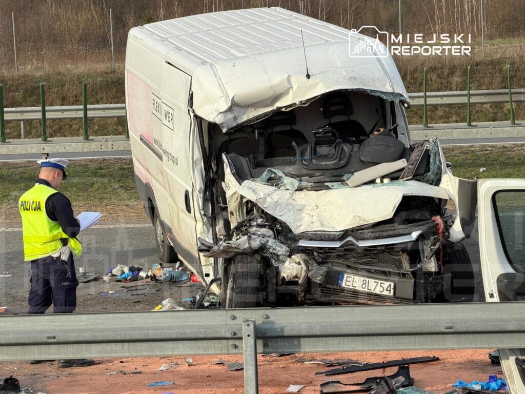 Policjant w kamizelce odblaskowej spisuje notatki obok rozbitego furgonu na poboczu drogi.