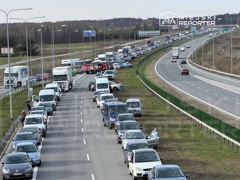 Ruch samochodowy utknął w korku na drodze ekspresowej, a kierowcy wysiadają z pojazdów na poboczu.