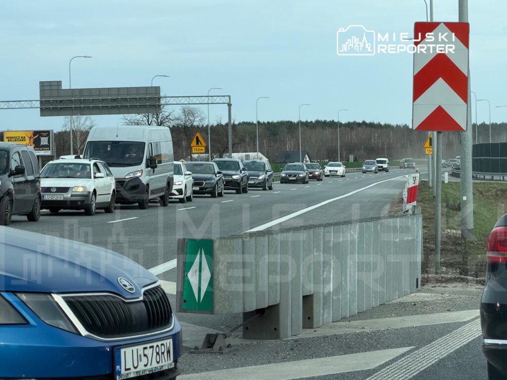 Ruch samochodowy na drodze ekspresowej, z widocznymi pojazdami stojącymi w korku oraz znakami drogowymi.