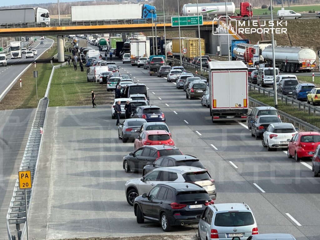 Kierowcy opuszczają samochody, czekając w długim korku na drodze, obok ruchliwej autostrady z ciężarówkami.