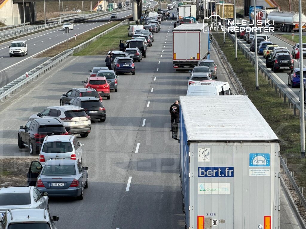 Korki samochodowe na drodze ekspresowej, z wieloma pojazdami stojącymi w zatorze, w tle widoczny ruch w przeciwnym kierunku.