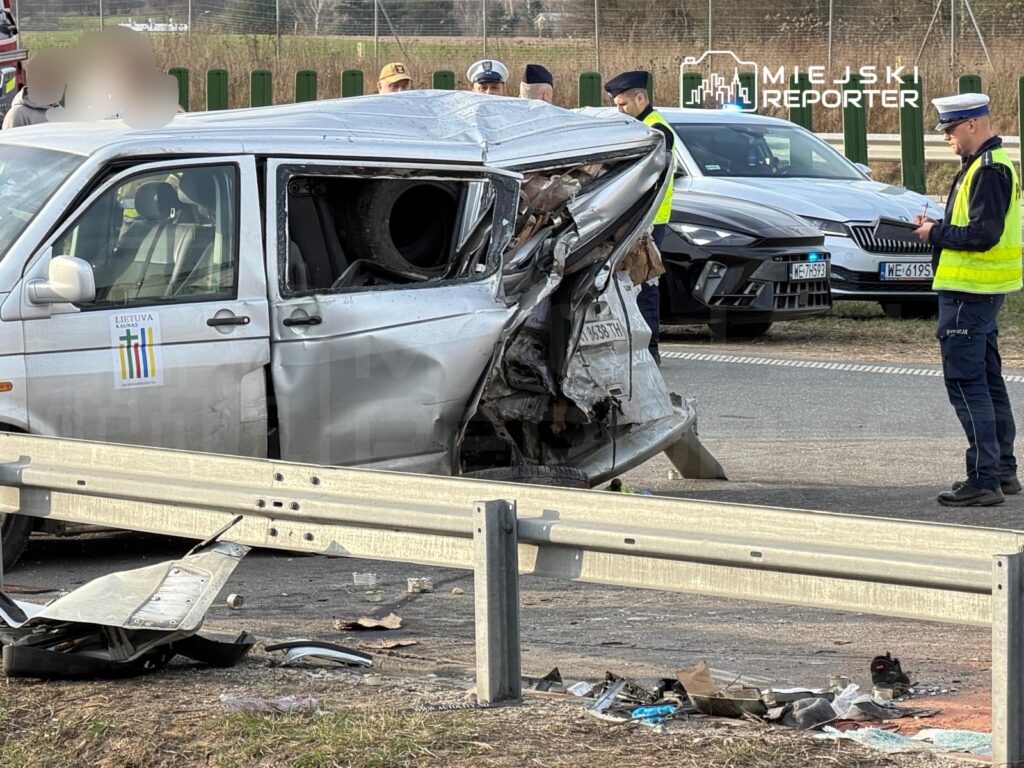 Rozbity samochód z uszkodzoną tylną częścią stoi przy drodze, obok grupy policjantów prowadzących dochodzenie.
