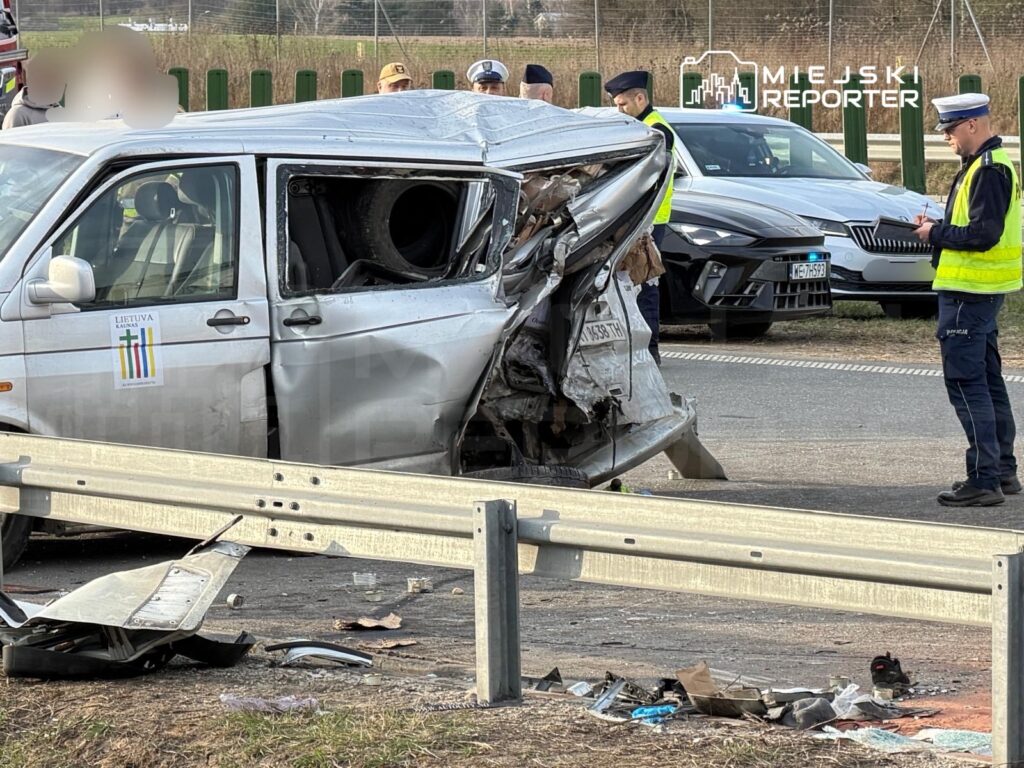 Uszkodzony samochód osobowy z zerwaną tylną częścią stoi przy drodze, obok grupy policjantów prowadzących czynności.