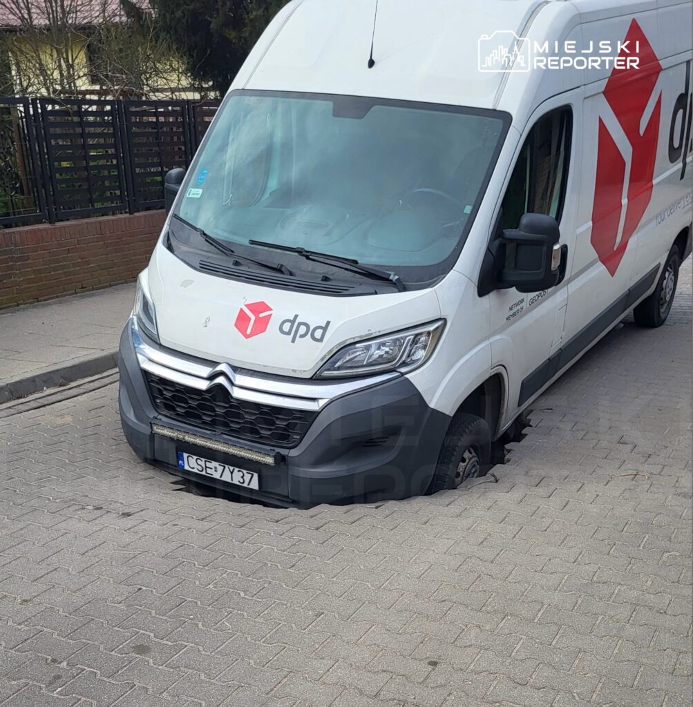 Dostawczy samochód z logo DPD utknął w zapadniętej nawierzchni na ulicy.