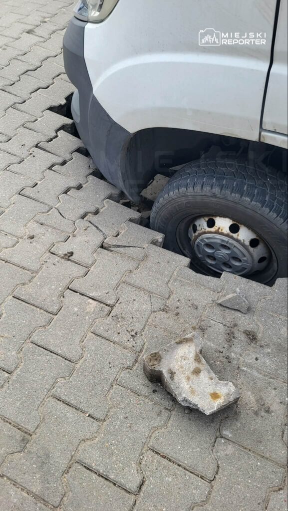 Samochód dostawczy utknął w pęknięciu na chodniku z kostki brukowej, obok leży fragment betonu.