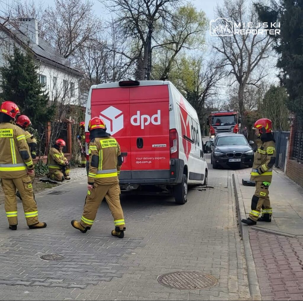 Grupa strażaków w mundurach przy pojeździe dostawczym DPD, sprawdzająca okoliczne tereny na osiedlowej ulicy.