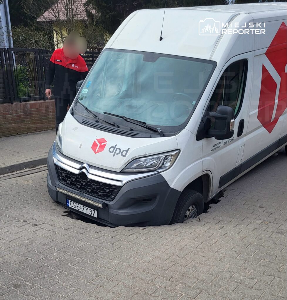 Furgonetka kurierska utknęła w zapadniętym chodniku, a kurier sprawdza sytuację obok pojazdu.