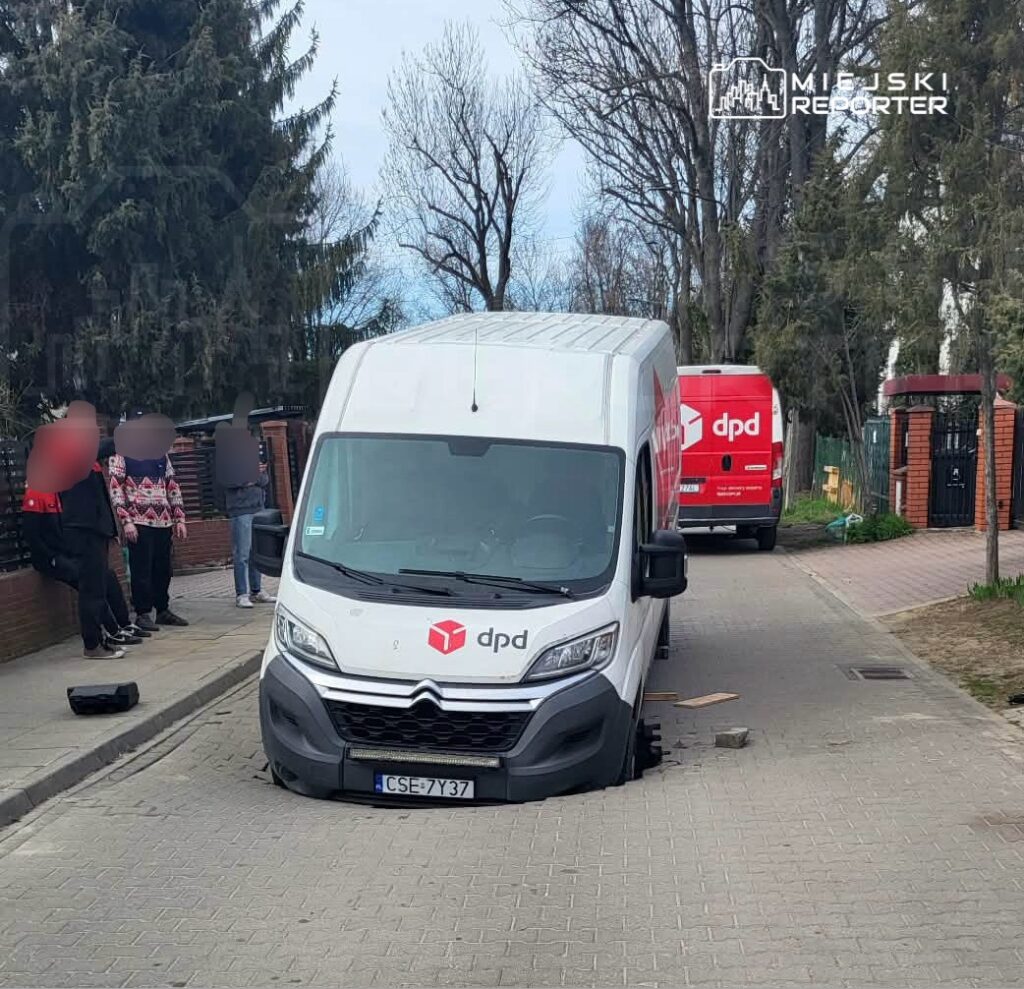 Samochód dostawczy DPD utknął w dziurze na chodniku, obok grupy osób obserwujących sytuację.