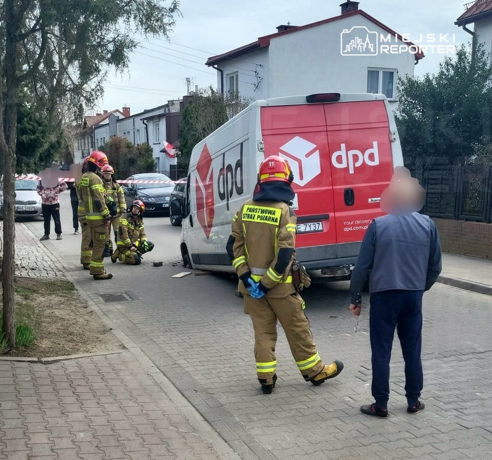 Grupa strażaków w mundurach ocenia sytuację obok dostawczego samochodu DPD na ulicy, a przechodzień obserwuje zdarzenie.