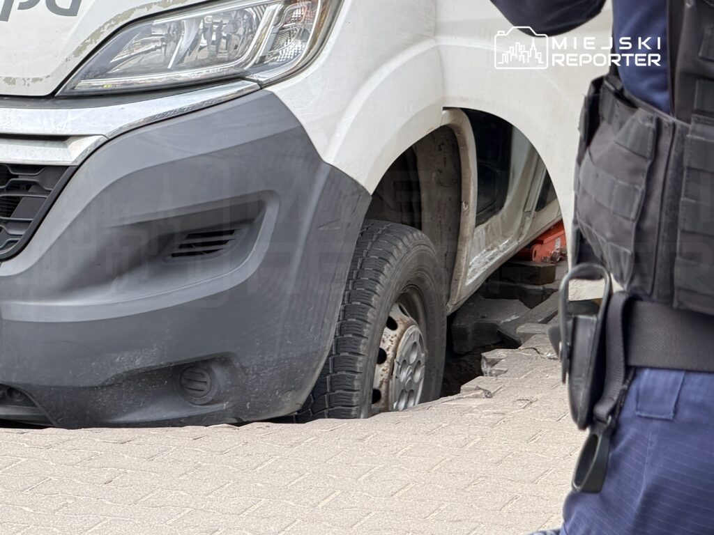 Samochód dostawczy utknął w zapadniętej nawierzchni na chodniku, obok stoi mężczyzna w mundurze.
