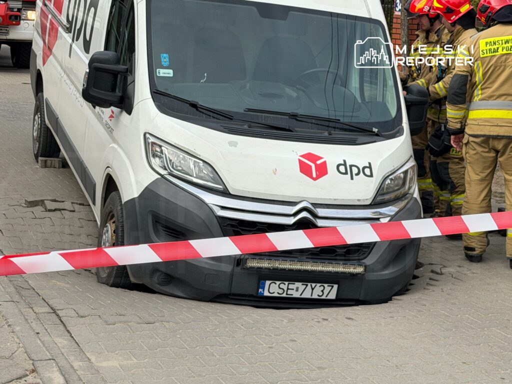 Samochód dostawczy DPD unieruchomiony na uszkodzonej nawierzchni, otoczony przez strażaków i taśmę ostrzegawczą.