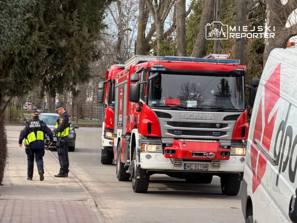 Strażnicy miejscy rozmawiają z kierowcą samochodu osobowego obok wozu strażackiego na miejskiej ulicy.