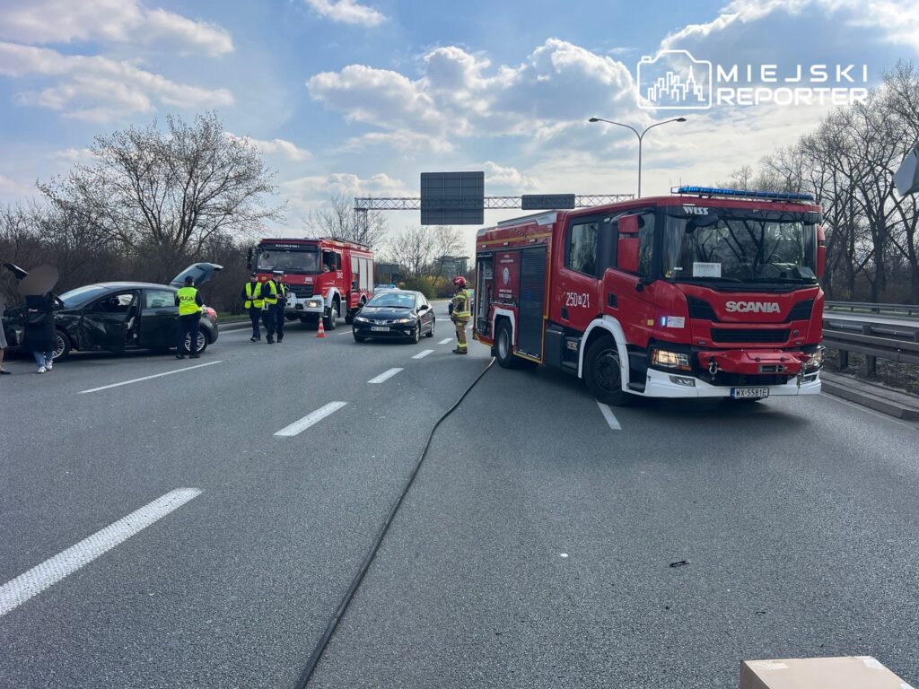Na drodze doszło do wypadku, w którym uczestniczyły dwa samochody; strażacy i policja zabezpieczają miejsce zdarzenia.
