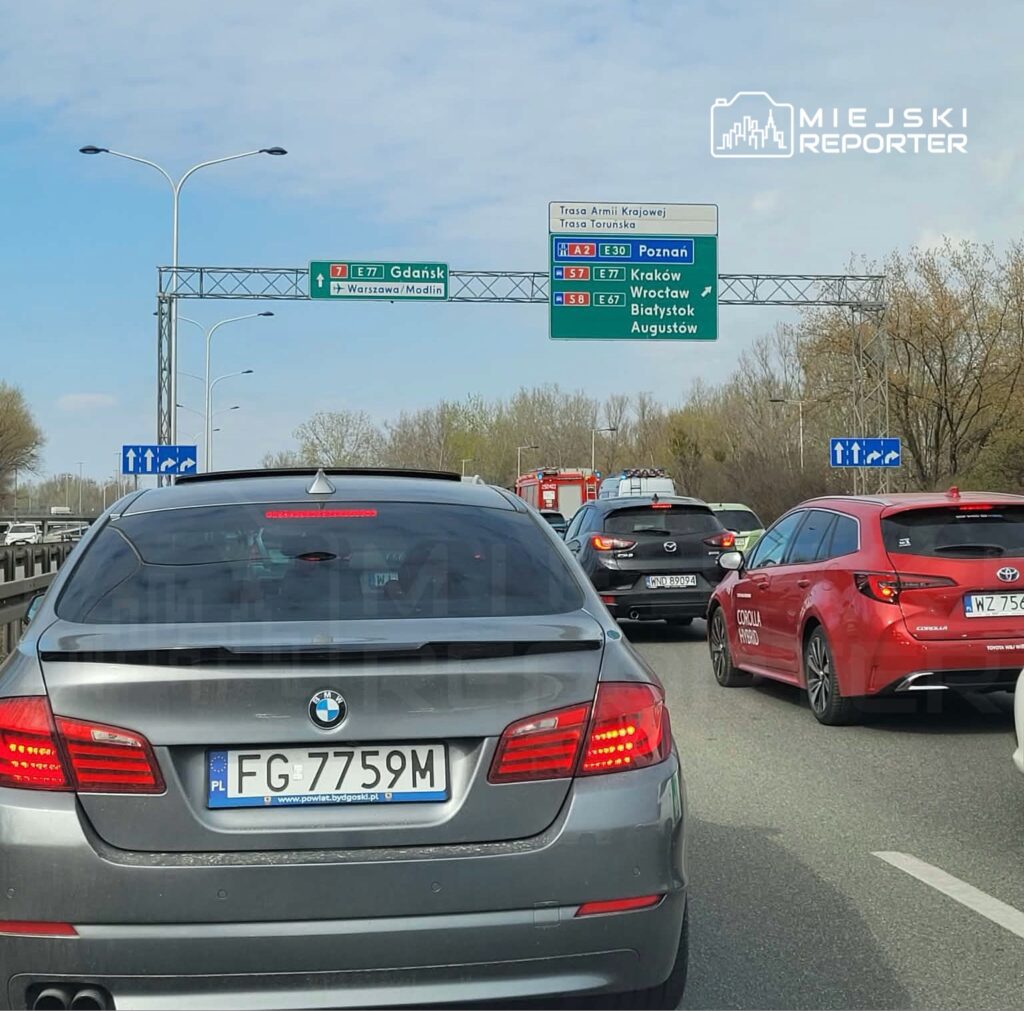 Ruch samochodowy na drodze ekspresowej z widocznymi znakami kierunkowymi do Gdańska, Poznania i Krakowa.