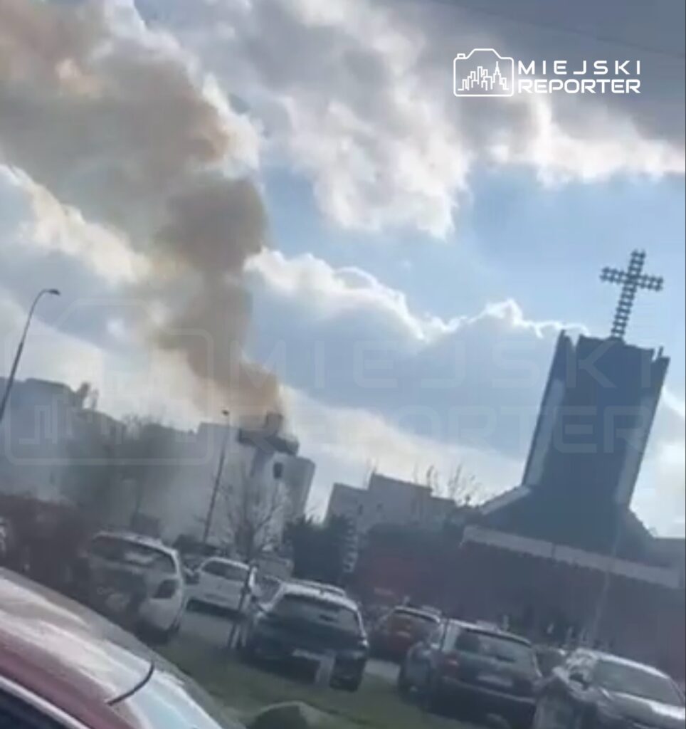 Gęsty dym wydobywający się z budynku w tle, w pobliżu kościoła z wysokim krzyżem.