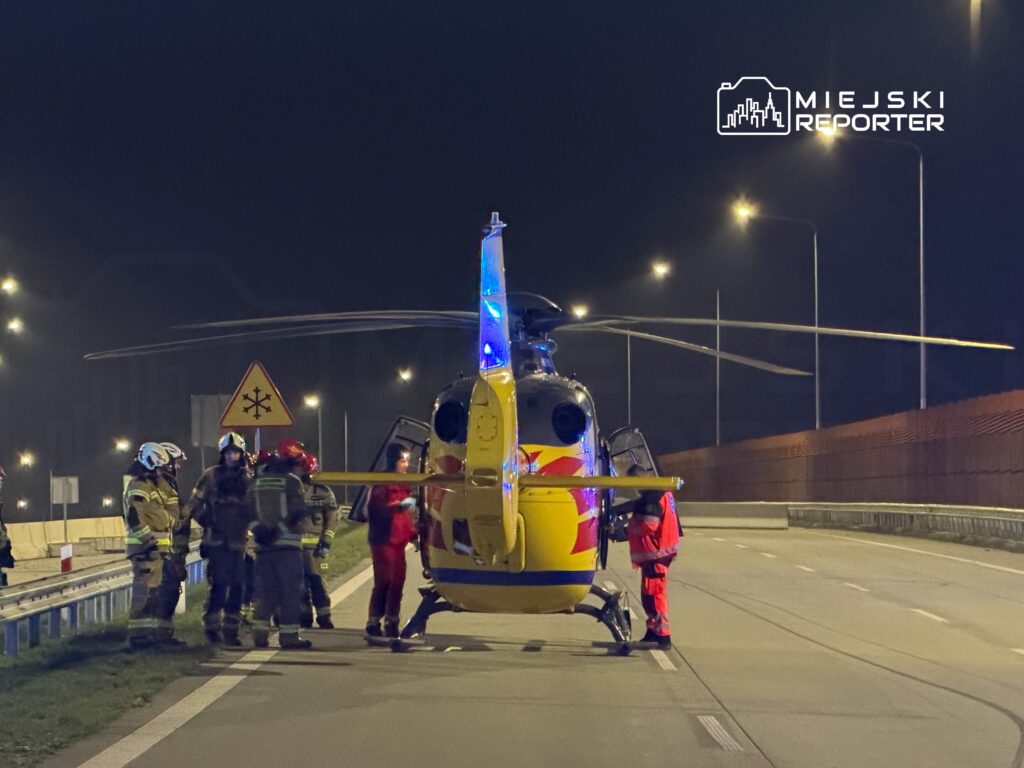 Grupa ratowników w odblaskowych strojach obsługuje śmigłowiec ratunkowy na drodze nocą.