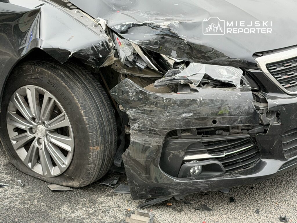 Uszkodzony przód czarnego samochodu osobowego z wgniecioną karoserią i uszkodzoną oponą.